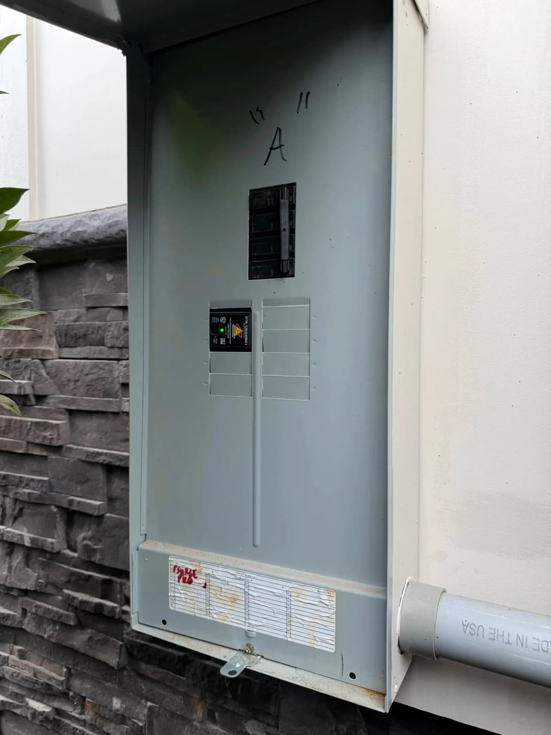 Residential electrical panel with circuit breakers mounted on a wall near stone facade.