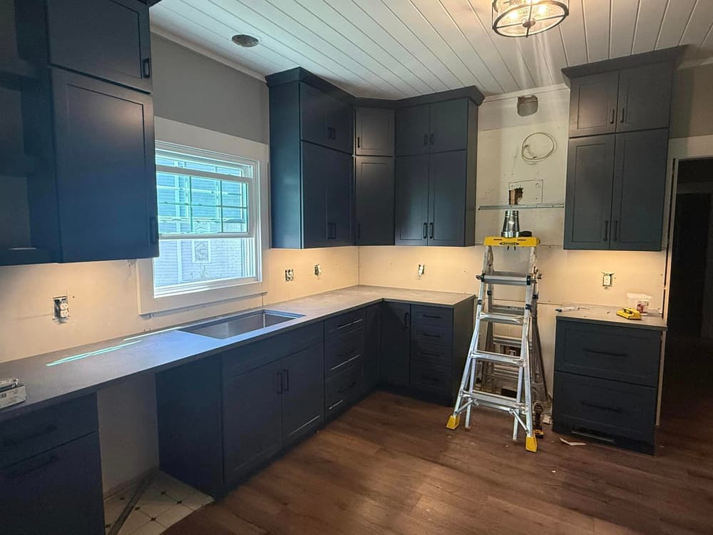 Modern kitchen renovation with navy cabinets, gray countertops, and a step ladder.