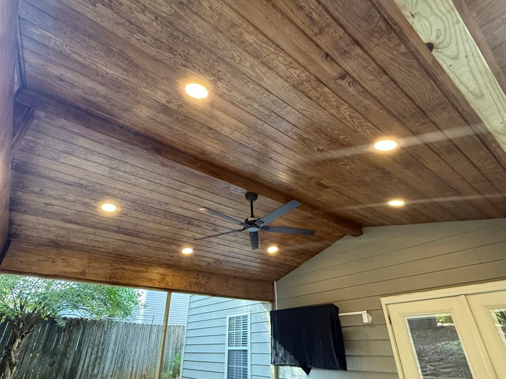 Stylish wooden ceiling with recessed lights and ceiling fan in a modern outdoor space.