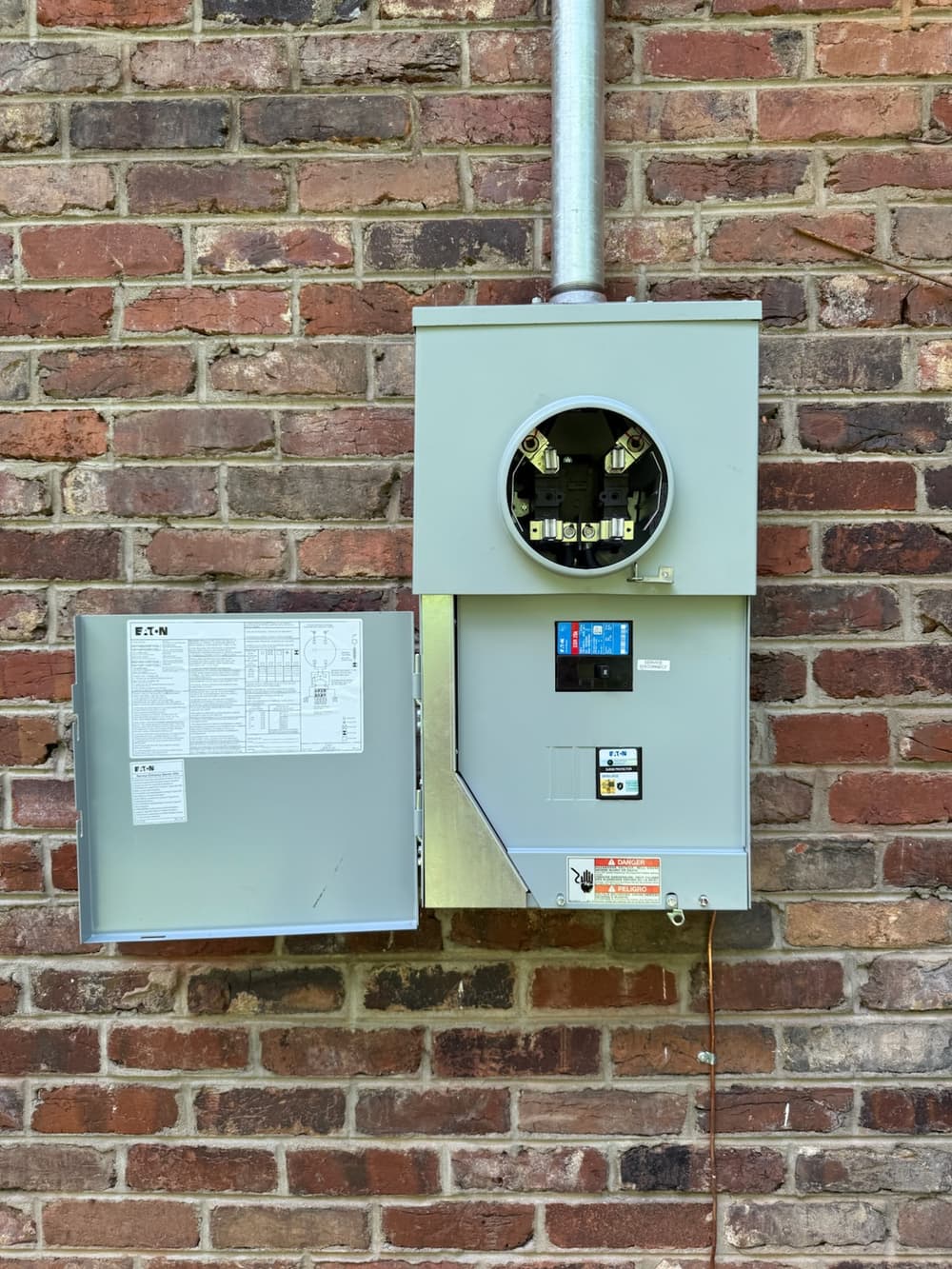 Electric meter mounted on a brick wall with a gray housing and labeled panel.