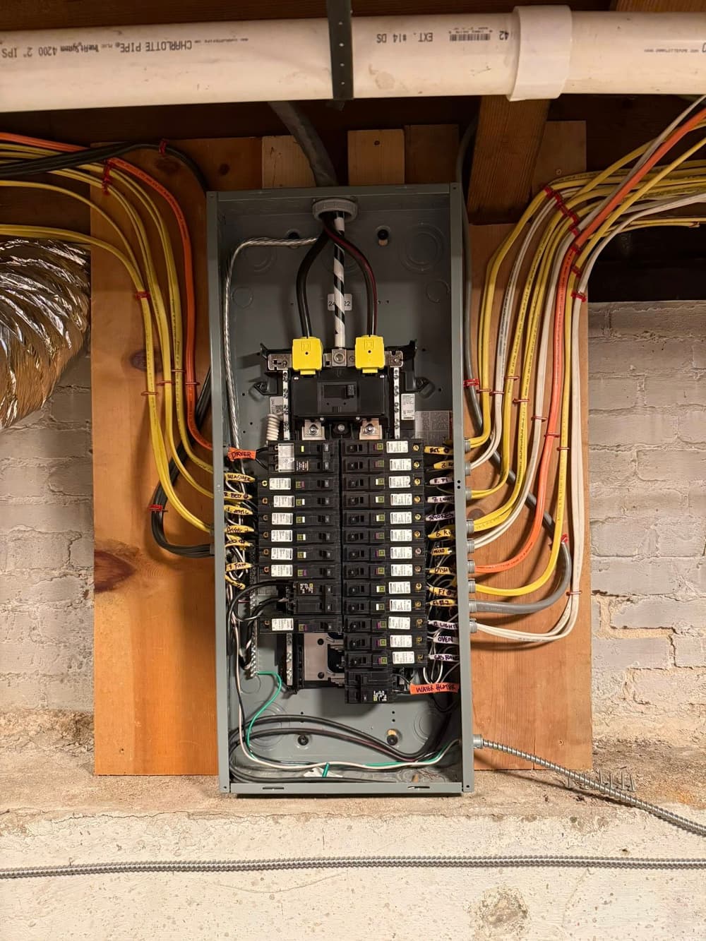 Electrical panel with multiple circuit breakers and wiring in a basement setting.